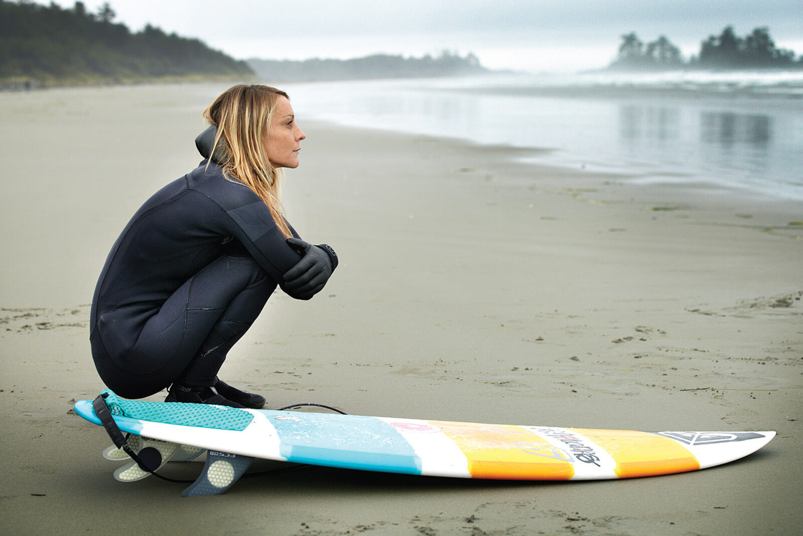 A woman beside her surfboard on a misty beach, from the Canadian Breast Cancer Foundation campaign