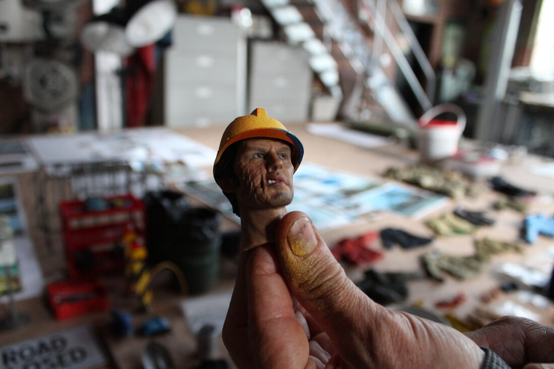 A hand-painted 1:6 scale construction worker figure held between fingers