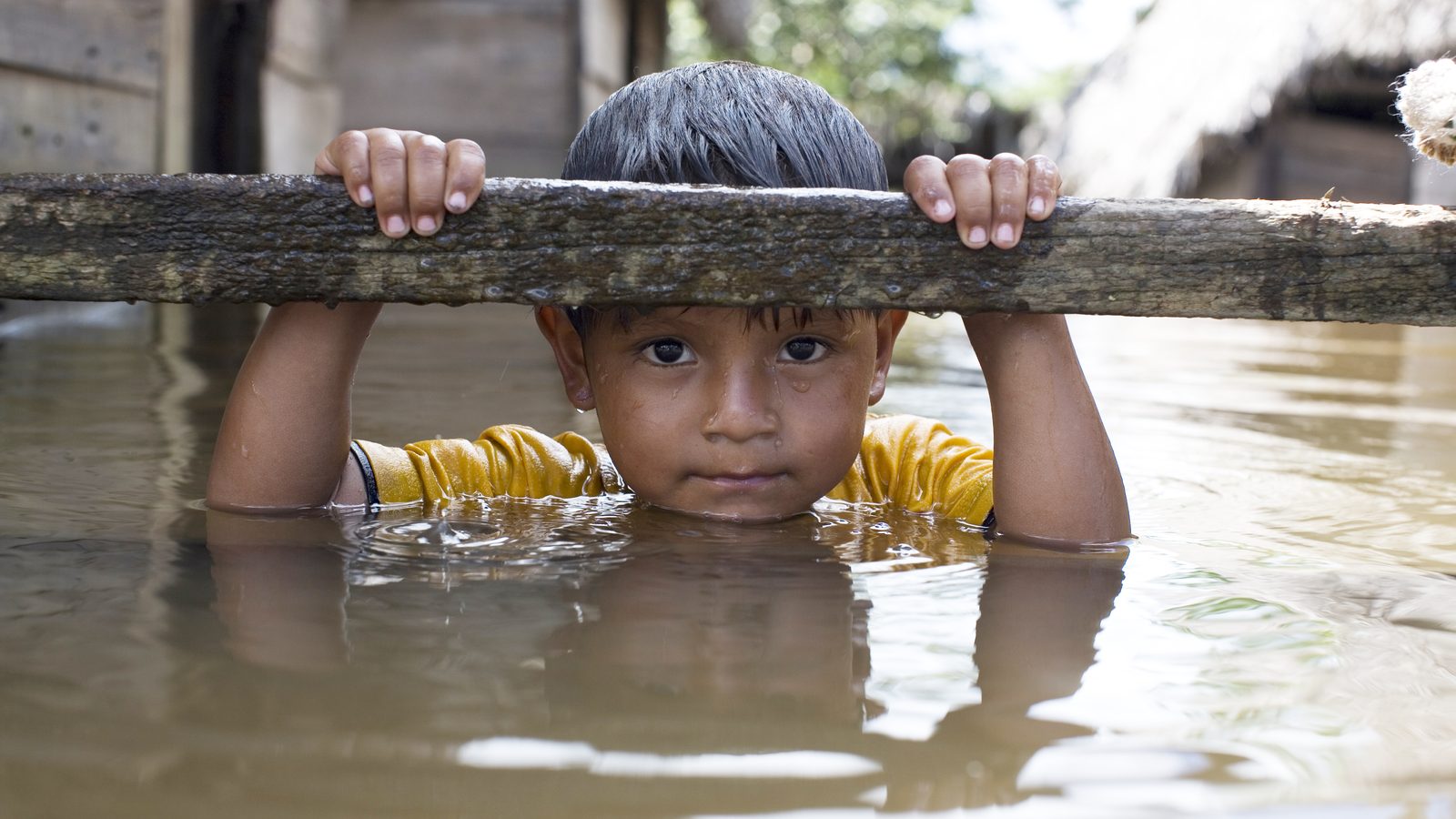 Un jeune garçon en équilibre sur une poutre de bois au-dessus des eaux de crue, regardant la caméra, une image tirée de la publicité télévisée d’UNICEF360