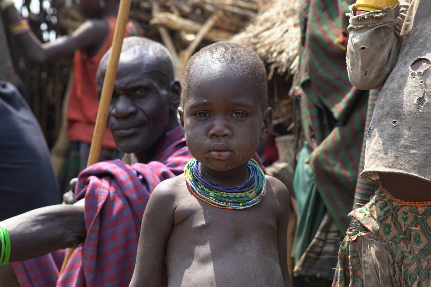 A young Karamojong child looking at the camera among adults in the village