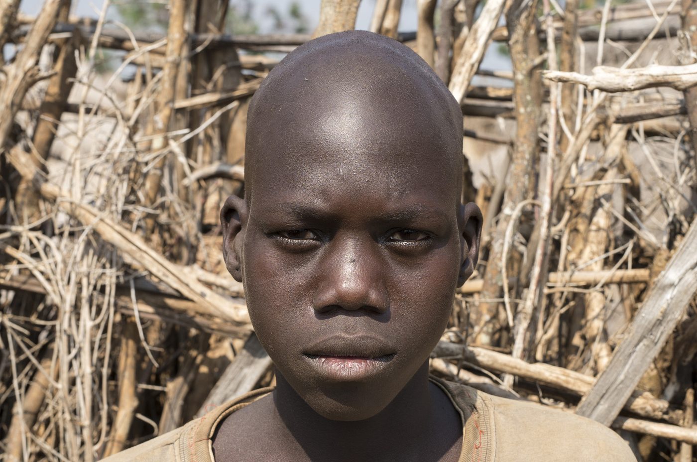 Lochap, a 12-year-old boy, standing before a woven stick fence and looking at the camera